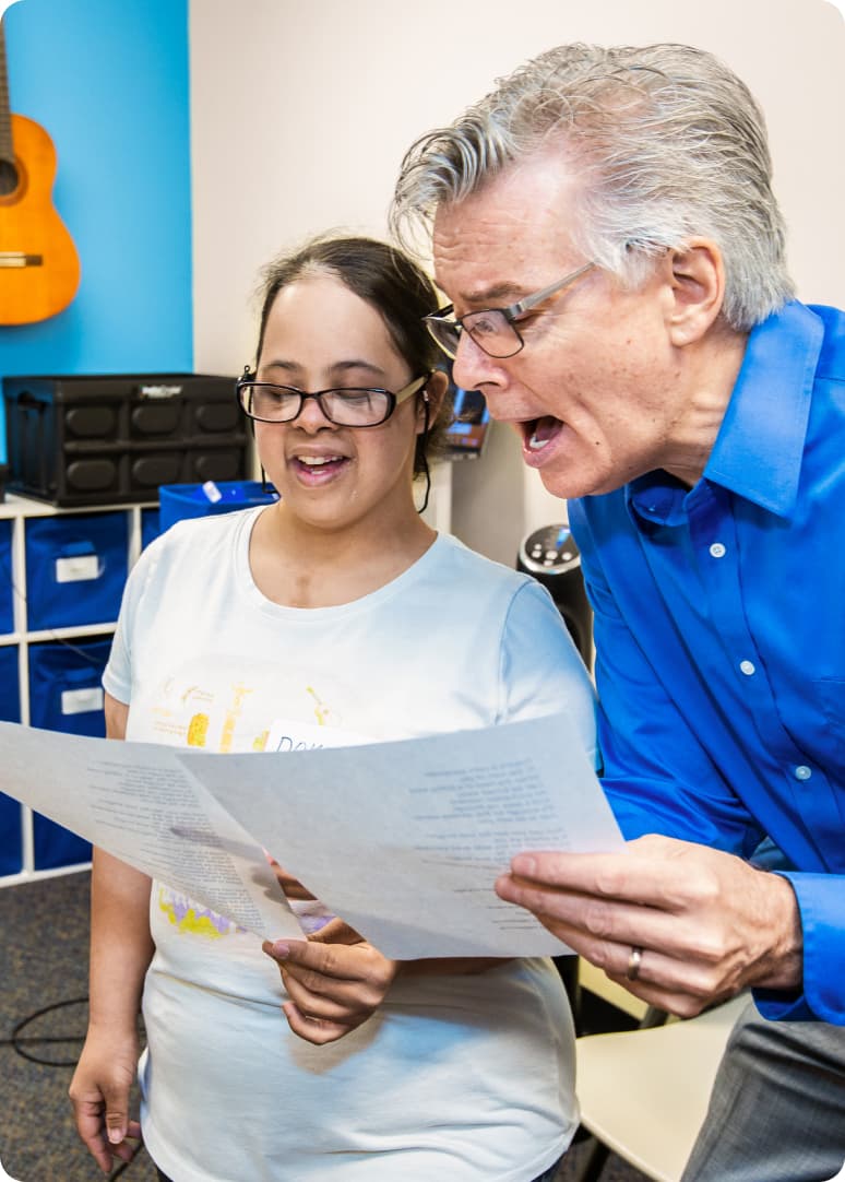 DMF Artistic Director Gerry sings with a DMF participant while reading lyrics off of a piece of paper