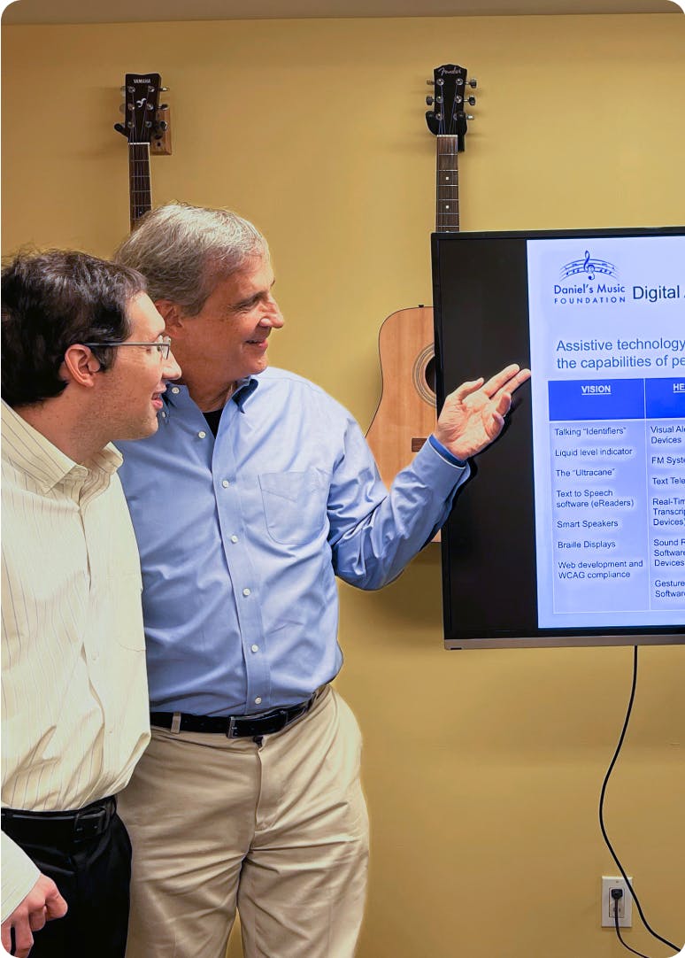Daniel and Ken Trush give a Disability Awareness presentation. Ken points to a screen with information about assistive technology