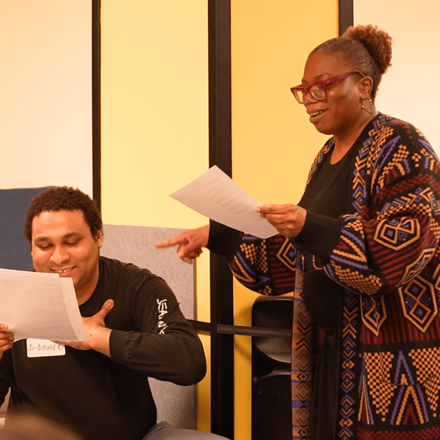 Photo of Cherelle reading from a sheet of lyrics, next to a student of hers