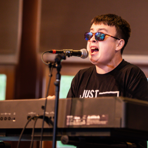 Image of Devin Gutierrez playing piano at Hello Inclusion. He is a black haired young man with dark glasses. 
