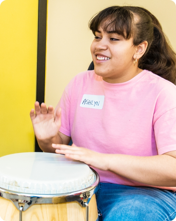 A smiling DMF participant uses their hands to play a beat on a drum