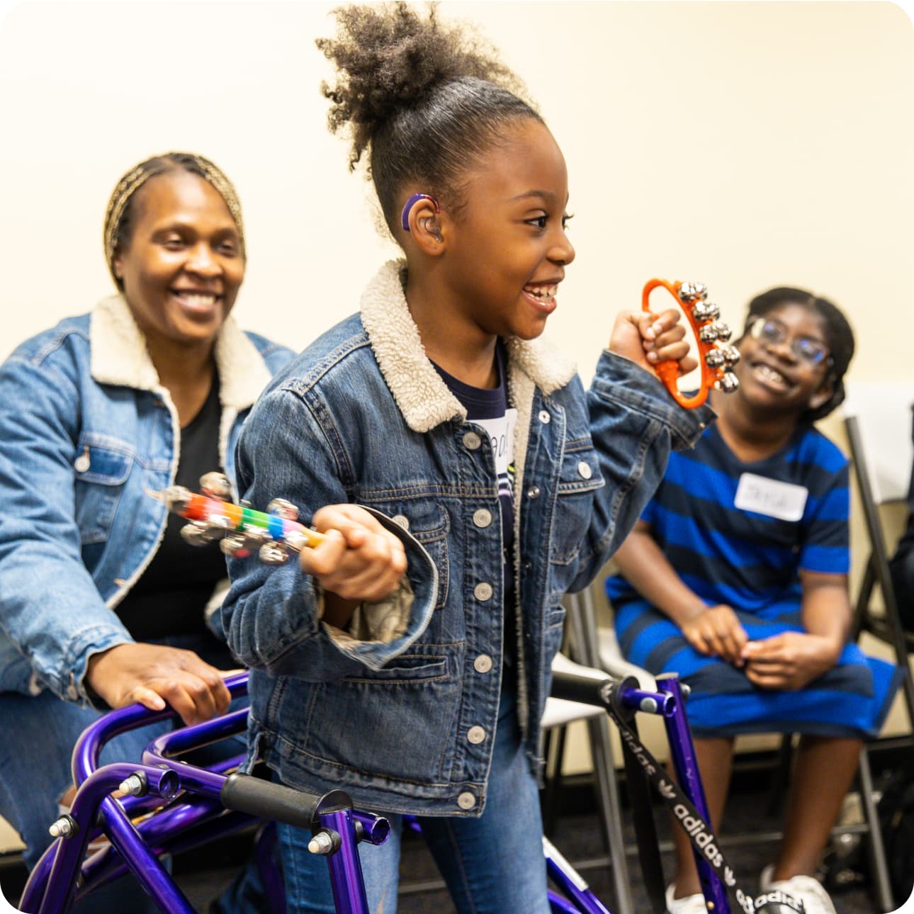 A DMF participant joyfully shakes instruments with jingle bells while 2 other participants smile at them