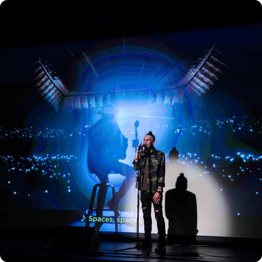 Danny Award recipient James Ian sings on stage with his original music video playing in the background