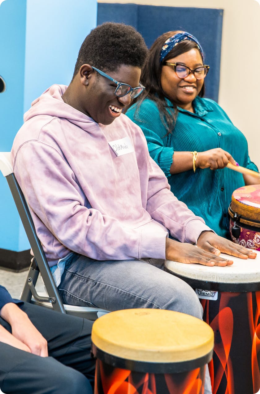 2 DMF participants share a laugh while playing drums