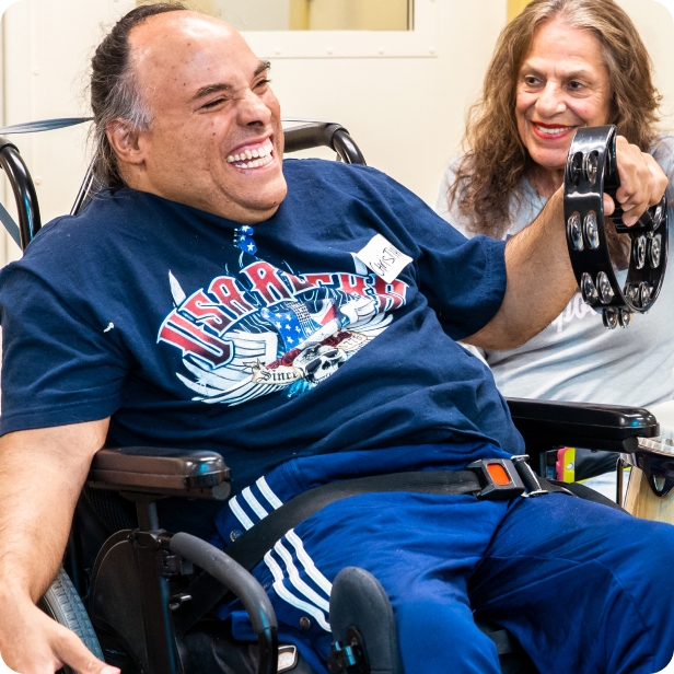 A DMF participant with a huge smile plays a tambourine next to another participant