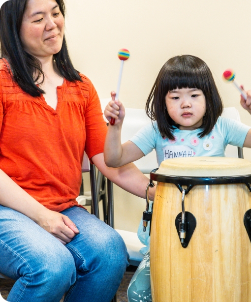 A DMF participant raises their arms with drum sticks while their parent smiles next to them