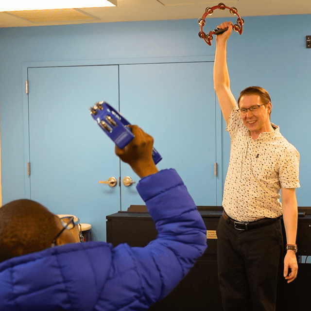 Photo of David Shaking a tamborine in front of a member in the classroom