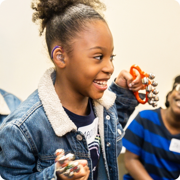 A DMF participant smiles while shaking instruments with jingle bells