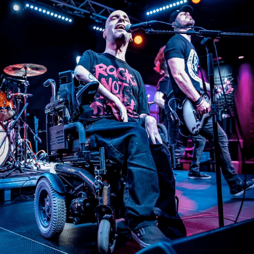 Photo of the lead singer of Corevalay singing. He is a Caucasian bald man in his 30s, using a wheelchair and wearing a black shirt