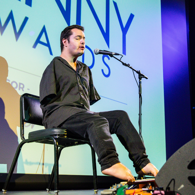 Image of George Dennehy performing at the Danny Awards. He is an armless man who is singing an playing guitar with his feet.