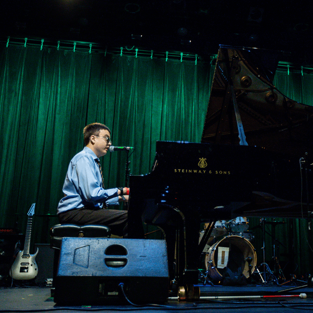 Photo of Devin Gutierrez playing piano at the Danny Awards. He is a blind man with dark hair, wearing a button down.