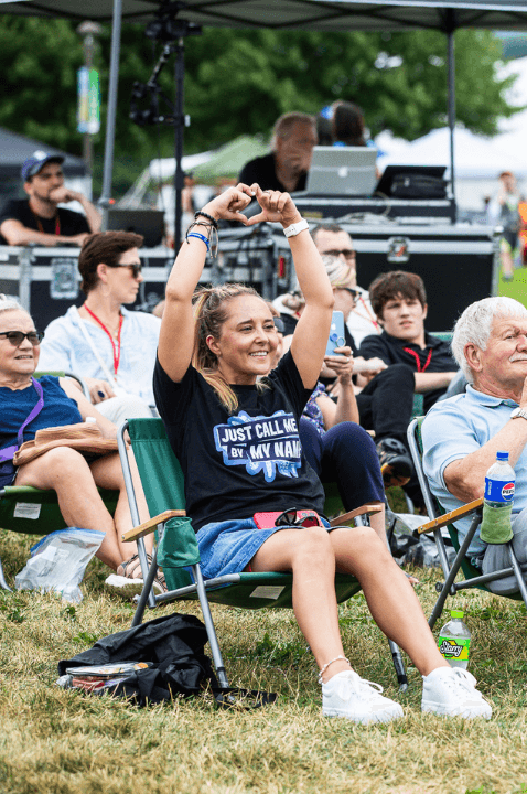 Photo of a woman sitting on a beach chair on the lawn at Hello Inclusion. She is making a heart with her hands in the air.