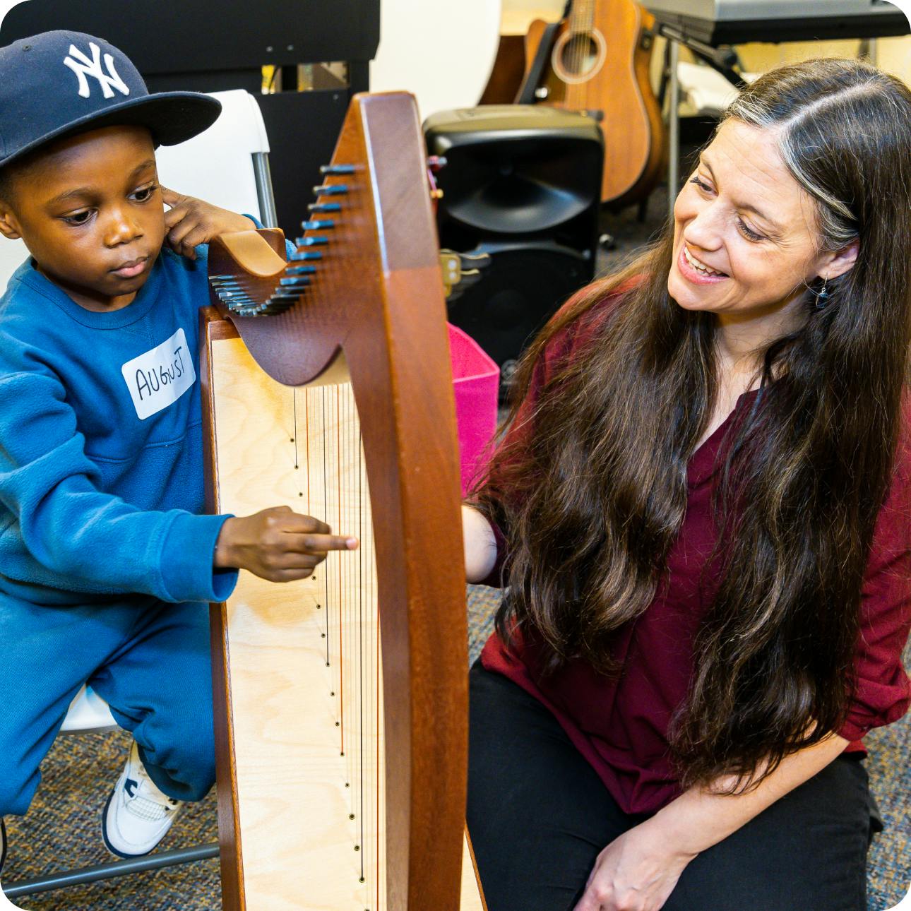 DMF Director of Teaching and Learning Juliana encourages a DMF participant to play the harp