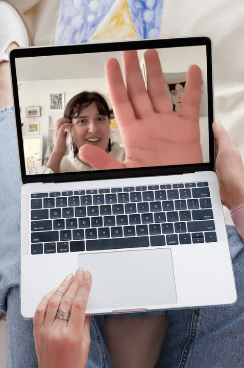 Photo of a woman watching an online class on their laptop. On the screen is instructor Stefani, offering a high five