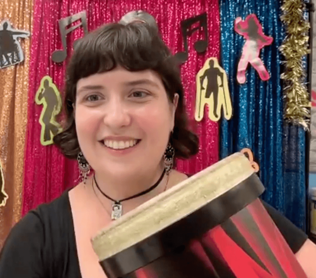 Instructor Stef playing the bongos and smiling during an online class