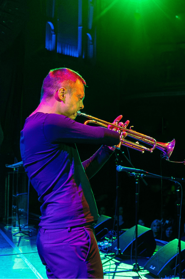 Photo of a man with one arm and short hair playing the trumpet on stage at the 2024 Danny Awards.