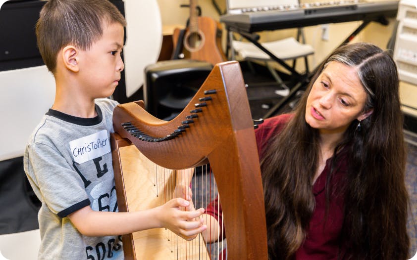 A DMF participant plays the harp with encouragement from DMF Director of Teaching and Learning Juliana