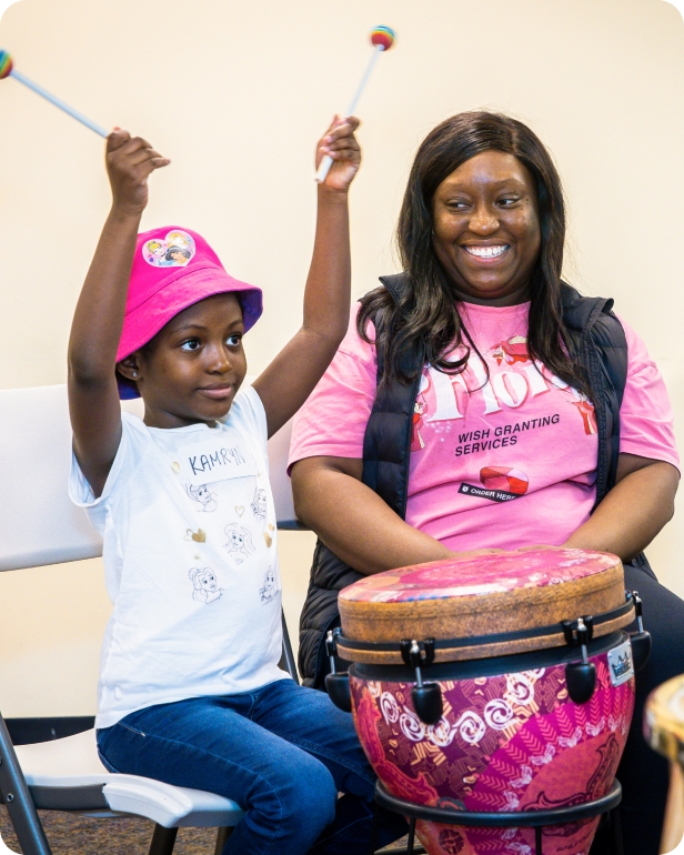 A DMF participant raises their drum sticks in the air while a parent smiles at them