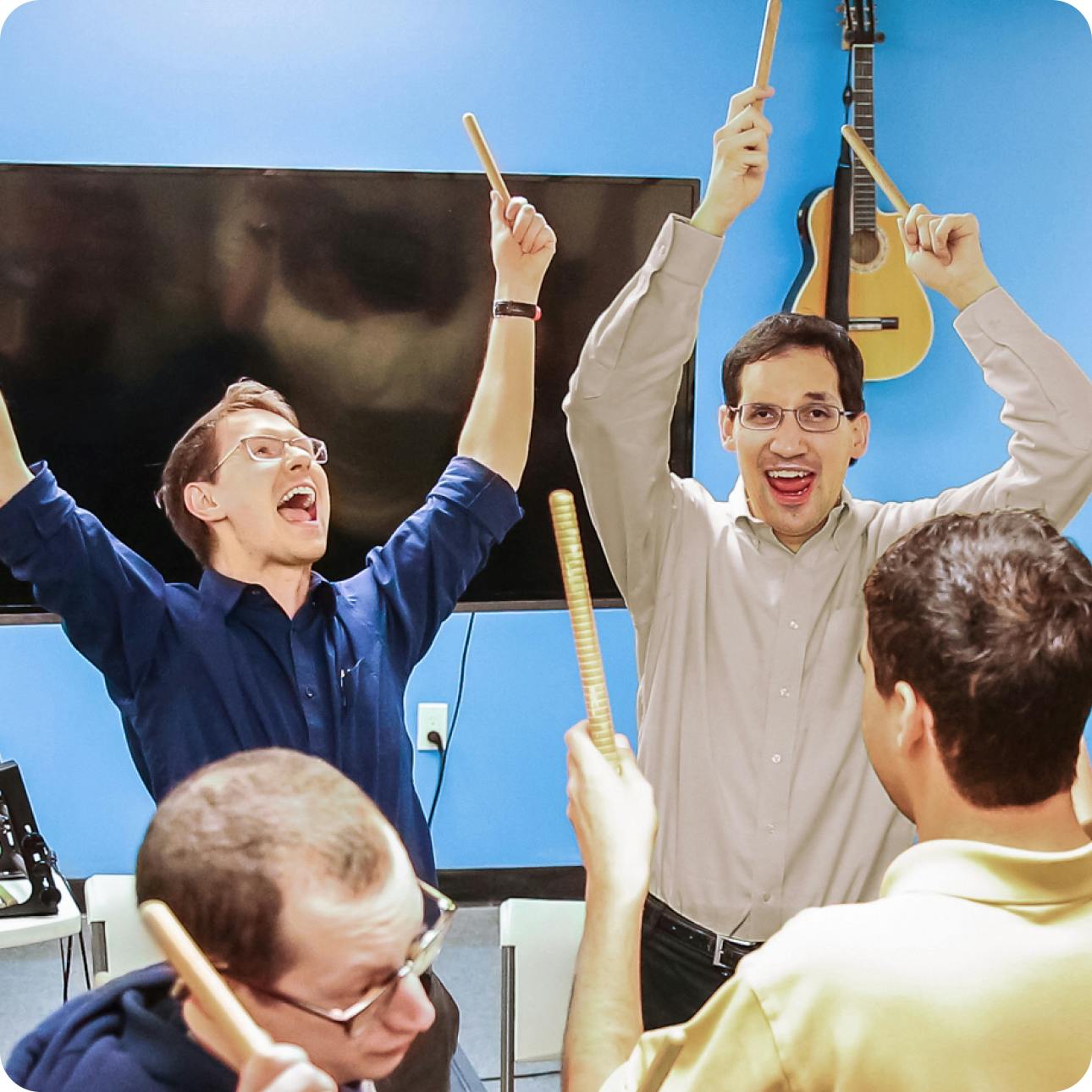 Daniel Trush and DMF Instructor David joyfully raise their drum sticks in the air in a group music class