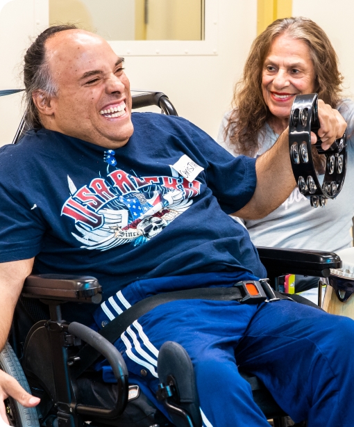 A DMF participant with a huge smile plays a tambourine next to another participant