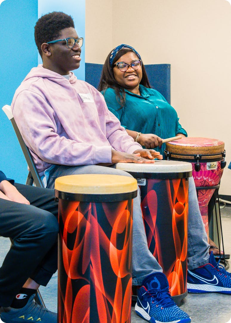 2 DMF participants laugh while playing colorful drums