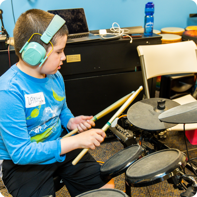 A DMF participant wearing bright blue headphones plays a drum set