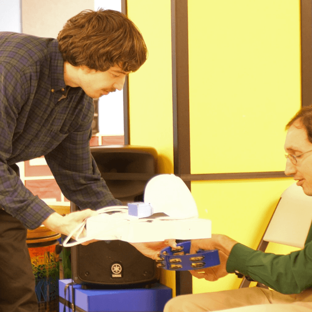 photo of Brian Culligan handing his adaptive instrument, the Masterpiece to Daniel Trush