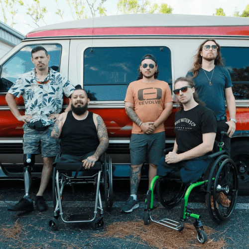 Photo of the band The Resilient posing in front of a van. The five members of the band are shown using wheelchairs or prosthetic limbs for mobility.